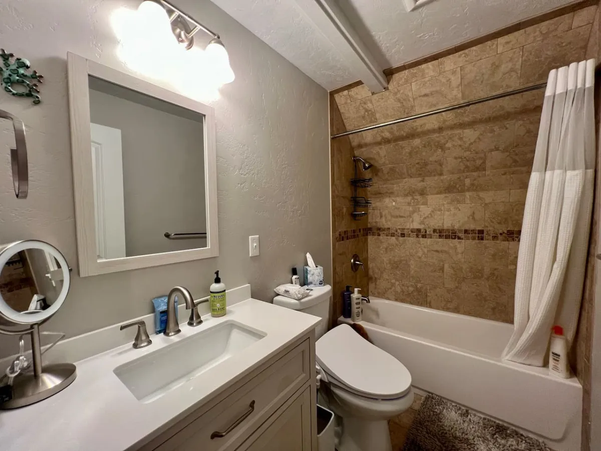 A stylish bathroom with a vanity and sink, large mirror, and a shower area adorned with natural elements decor. The overall feel is refreshing and calming, indicating quality fixtures and a touch of luxury.