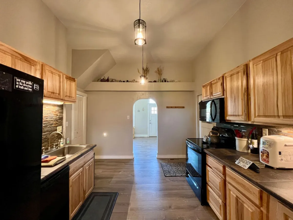A warm, homey kitchen interior featuring kitchen cabinets, a sink, an archway leading to another room, and a prominent light fixture. The open layout suggests an easy flow between the kitchen and adjacent living spaces, ideal for social cooking and entertaining.