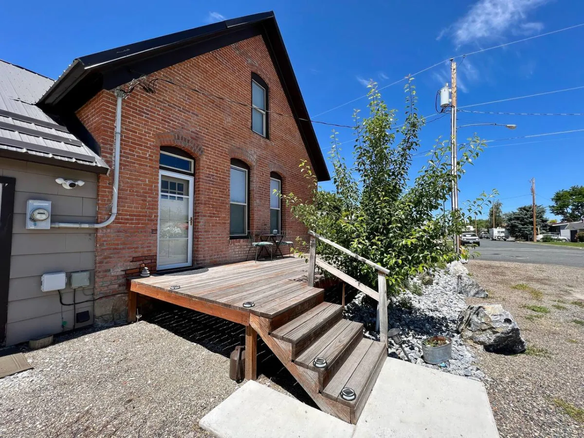 This exterior view focuses on the brick facade and wooden steps bordered by greenery and a seating area, capturing the intimate outdoor spaces designed for relaxation, morning coffee, or evening gatherings.